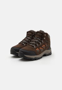 Brązowe buty trekkingowe z szarymi akcentami, tekstylną cholewką, wytrzymałą podeszwą, pomarańczowymi detalami i metalowymi oczkami na sznurowadła. Półwysoka konstrukcja dla wsparcia kostki.