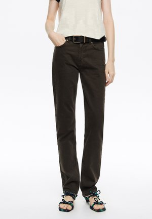 Pantalones de pierna recta marrón oscuro hechos de algodón, con bolsillos laterales y un cinturón. Combinados con sandalias adornadas con tiras coloridas.