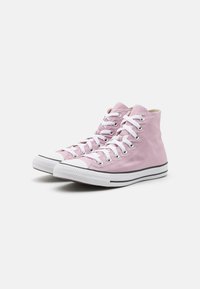 Zapatillas altas de lona en rosa claro con cordones blancos, suela a rayas en blanco y negro, y ojales de metal. Punta de goma plana.