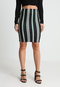 Černá úzká sukni s rib strukturou a vertikálními pruhy v zelené a bílé, doplněná černými sandály na podpatku se cvočky.
