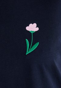 Mørkeblå bomullsskjorte med brodert rosa blomst med grønne blader på venstre side. Myk tekstur, uformell design.