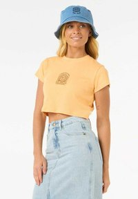 Camiseta naranja recortada de manga corta con un pequeño diseño impreso. Combinada con una falda de mezclilla azul clara y un sombrero tipo cubo azul.
