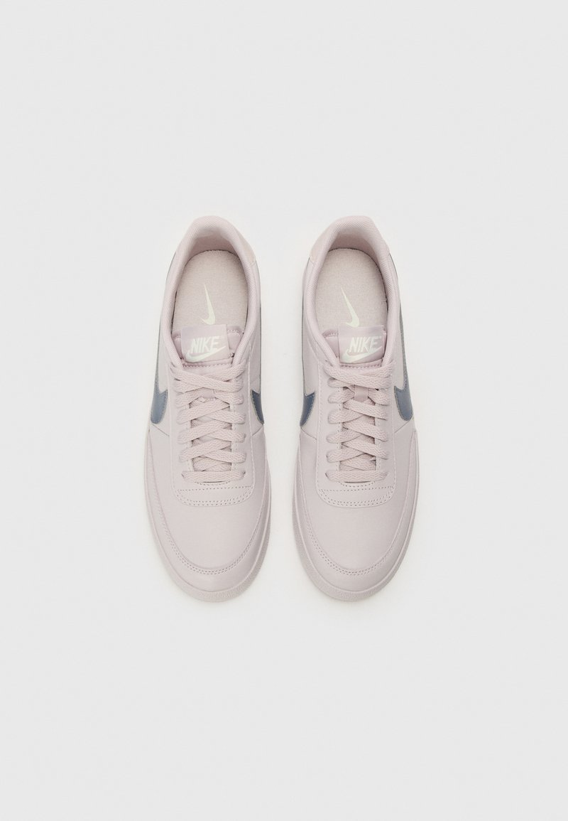 Sneaker Nike rosa chiaro con una texture liscia, swoosh grigio, lacci piatti e suole imbottite, caratterizzati da un design minimalista.