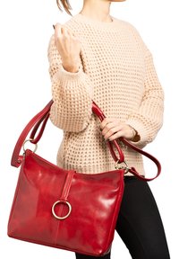 Sac à main en cuir rouge avec une finition brillante, présentant un accent matériel circulaire de couleur dorée et une bandoulière réglable.