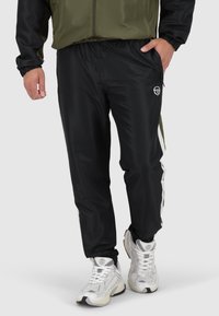 Pantaloni sportivi neri in materiale morbido, con vita elastica, tasche laterali e un logo bianco sulla coscia sinistra.