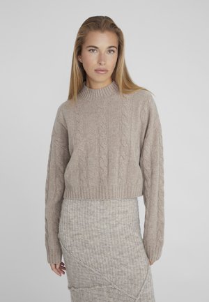 Pull en maille cable beige avec un col montant et des manches longues, présentant des poignets et un ourlet côtelés. Texture douce avec un design court.