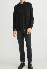 Černá bomber bunda na zip, doplněná černým tričkem a tmavě šedými úzkými kalhotami, zakončená elegantními černými botami.