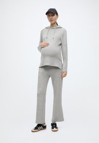 Gaiši pelēka kapuce ar priekšējo kabatu un auklu, kopā ar saskanīgām izplešamām biksēm. Valkāts ar melniem un baltiem sporta apaviem un cepuri.