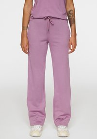 Lila sweatpants met een trekkoord tailleband, relaxte pasvorm en zachte textuur, gecombineerd met wit en beige patroon sneakers.