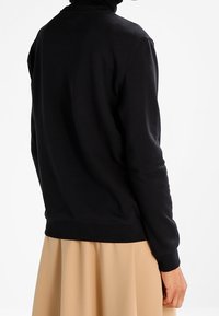 Svart sweatshirt gjord av mjukt tyg, med ribbad halsringning och ärmar. Passformen är avslappnad, med en midja som sitter vid höfterna.