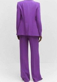 Traje morado con blazer entallado que tiene una espalda ligeramente acampanada y pantalones de pierna ancha, confeccionado en una tela suave con detalles mínimos.