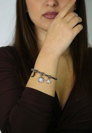 Silver charm bracelet featuring a moon, sun, and star. The bracelet has a smooth texture and a flexible design with circular links.