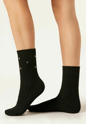 Chaussettes noires à côtes avec des poignets, ornées d'accents en cristal décoratifs sur les côtés. Fabriquées à partir d'un matériau doux et extensible.
