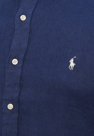 Marineblå lin skjorte med knapper og hvit logo brodert. Har standard knappelukking og teksturert stoff.