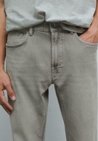 Jeans in denim grigio con una vestibilità slim, dotati di tasche frontali, chiusura con bottone e sbiaditure sottili sulla stoffa.