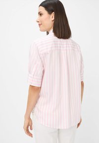 Light pink and white striped short-sleeve shirt with a rounded hem and back yoke detail, featuring buttoned rolled cuffs.