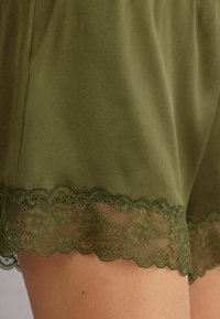 Olivgröna shorts med en mjuk, slät textur, prydda med en scalloped spetsdetalj i matchande mörkgrön vid nederkanten.