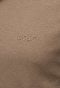 Tissu taupe avec le mot "BOSS" embossé en couleur assortie, centré sur la surface.