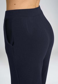 Pantaloni alti blu navy con tasche laterali, realizzati in un tessuto textured. Presentano un design aderente che si restringe alle caviglie.