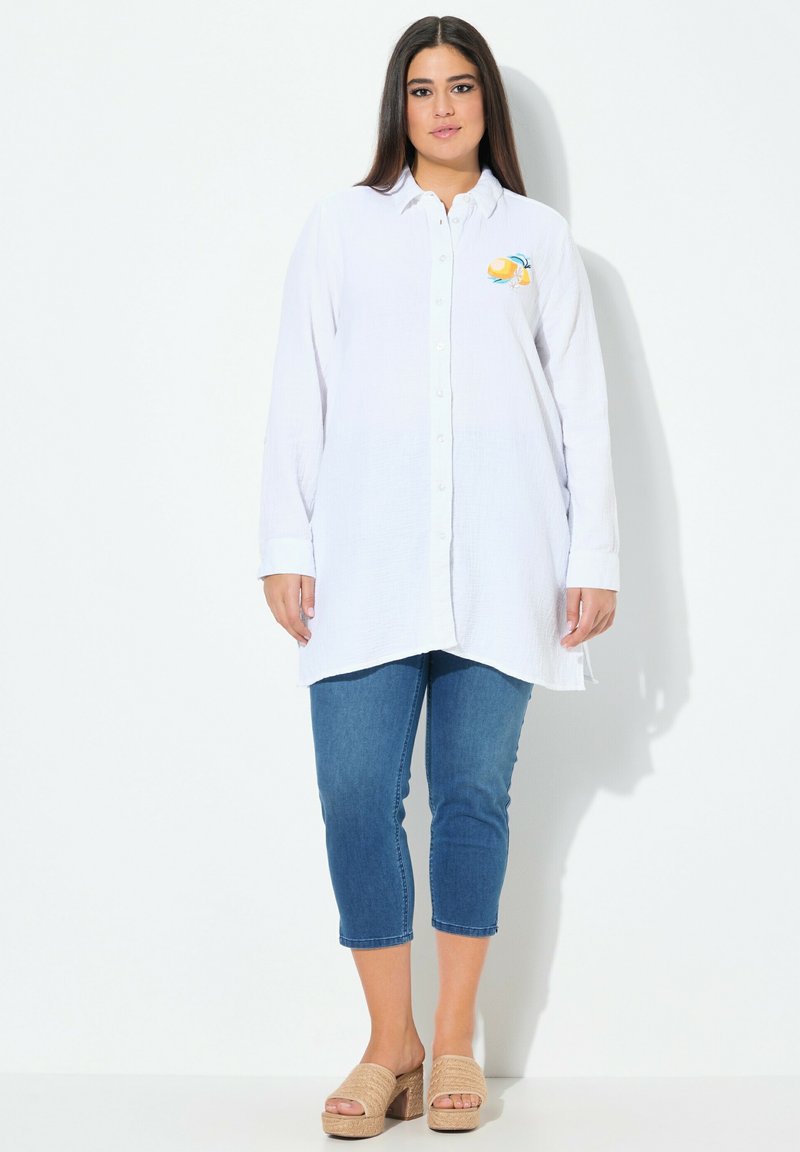 Camicia bianca con bottoni, realizzata in un tessuto texture, con un design ricamato a forma di limone sul lato sinistro del petto. Abbinata a jeans cropped blu e sandali color carne.