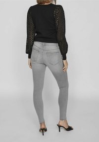 Top negro con mangas de encaje abullonadas, combinado con jeans ajustados grises. La ropa presenta un diseño ceñido y detalles de calado en las mangas.