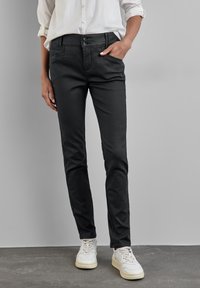 Musta, slim-fit housut, joissa on sileä pinta, kaksi etutaskua ja kaksoispainon suljenta, yhdistetty valkoisiin lenkkikenkiin.