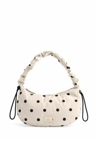 Beige taske med prikker og en samlet håndtag, lavet af blødt stof. Har en lynlås lukning og en lille logo lap. Sorte prikker er jævnt fordelt.