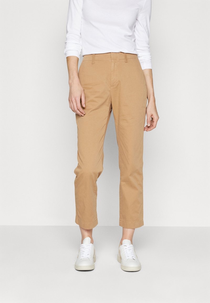 Pantalons en coton beige chino avec une coupe slim, longueur cropped, et poches avant. Assortis à des baskets blanches et un haut à manches longues.
