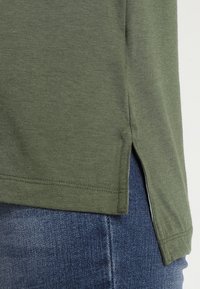 Olivgrön t-shirt med sidoflik, tillverkad av mjukt tyg, med rak passform och synliga söm detaljer.