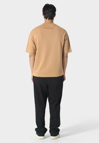 Písková bavlněná košile s krátkým rukávem a volným střihem, spojená s černými kalhotami s vysoce kvalitním střihem a elastickými manžetami.