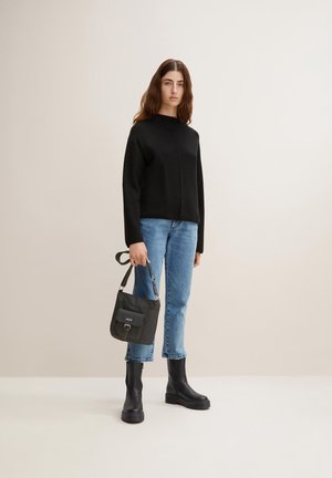 Maglione nero corto, jeans dritti blu chiaro, stivali neri alla caviglia e una piccola borsa a tracolla grigia con tasca frontale.