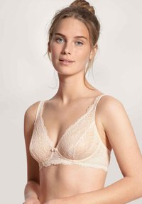 Kant BH in lichtnudetint met een diepe decolleté, geschulpte randen en een strikje in het midden. Verstelbare bandjes verbeteren de pasvorm.