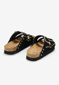 Sandalias de plataforma de ante negro con tachuelas doradas y una hebilla decorativa. Plantilla de corcho con suela texturizada para mayor agarre. Diseño abierto.