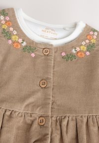 Beige corduroy baby dress with wooden buttons and embroidered floral patterns in orange, yellow, pink, white, and green around the neckline.