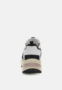 Sneaker bianco e nero con tomaia in tessuto, dettagli rosa, suola spessa e logo "GUESS" sul tallone. Presenta una linguetta per indossarla facilmente.