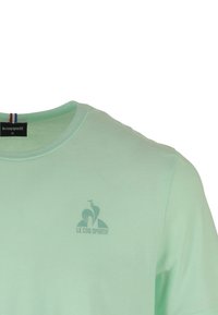 T-shirt verde menta realizzata in morbido cotone, con scollatura tonda e un logo sottile sul petto, arricchita da un accento tricolore sul colletto.