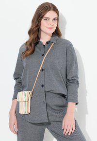 Camisa gris de botones con mangas largas, fabricada en tejido texturizado y con cuello. Combinada con un bolso cruzado de tejido con rayas multicolores.