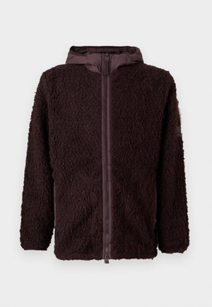 Giacca in pile marrone, shaggy, con zip frontale, cappuccio e tasche laterali. Presenta un tessuto liscio, probabilmente resistente all'acqua, sul cappuccio e nell'area della zip.