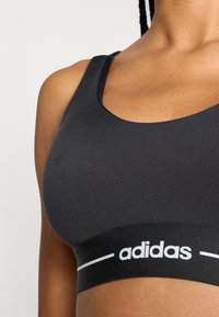 Zwarte sportbeha met een ronde halslijn, gemaakt van gladde stof. Heeft een contrasterend wit logo en band, die het minimalistische ontwerp benadrukken.