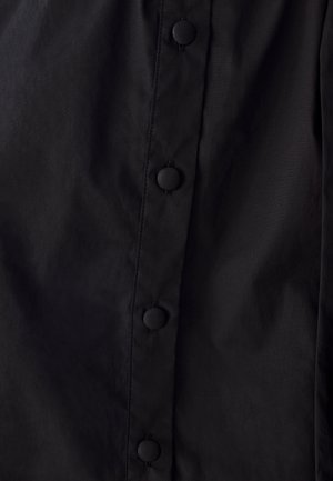 Čierna látka s hladkým povrchom, obsahujúca vertikálny rad okrúhlych čiernych gombíkov. Materiál je ľahký a mierne lesklý.