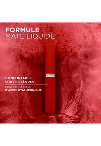 Rouge à lèvres liquide rouge dans un tube élégant avec une finition mate. Il présente un logo argenté et revendique des propriétés hydratantes grâce à l'acide hyaluronique.