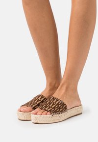 Brown espadrille sandals with open toe design, featuring patterned fabric upper and woven jute sole. Flat with a slight elevation.