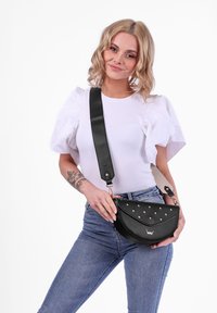 Černá kabelka z umělé kůže ve tvaru půlměsíce, se zlatými cvočky vpředu, odnímatelným popruhem a hladkým povrchem.