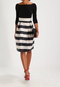 Haut noir sans manches associé à une jupe jusqu'aux genoux avec des rayures horizontales noires et blanches. Des talons rouges à lanières achèvent le look.