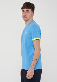Maglietta blu a maniche corte con scollatura rotonda, caratterizzata da un accento verde neon sulle maniche e un piccolo logo sul petto. Tessuto morbido.
