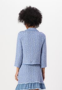 Blå tweed-blazer med trekvartslange og krage, kombinert med et matchende skjørt som har en frayed denim-kant.