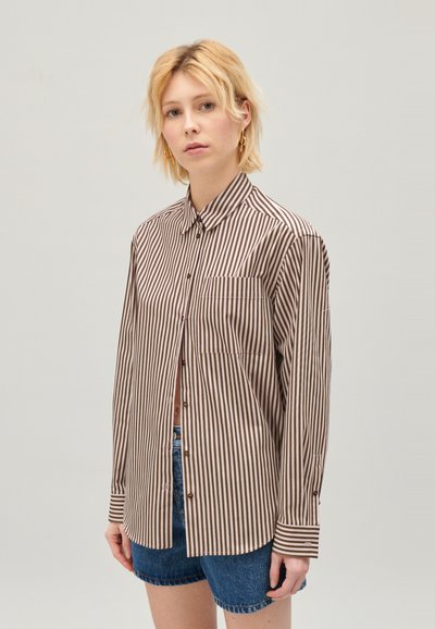 Csíkos, barna és törtfehér gombos ing, mellzsebbel, hosszú ujjal és klasszikus gallérral. Farmer shorts-al viselve.