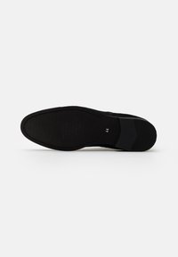 Suela de zapato negra con superficie de goma texturizada, tacón rectangular y indicación de tamaño numérico (44) cerca del tacón. Diseño plano y minimalista.