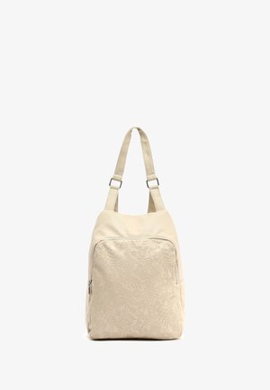 Sac en cuir beige avec un motif floral texturé, doté de bretelles réglables et d'une poche zippée à l'avant. Forme rectangulaire compacte.