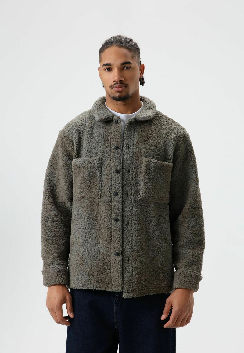 Fleece shirt jacket in muted green with a snap button front, two chest pockets, and a soft texture; features a collar and long sleeves.